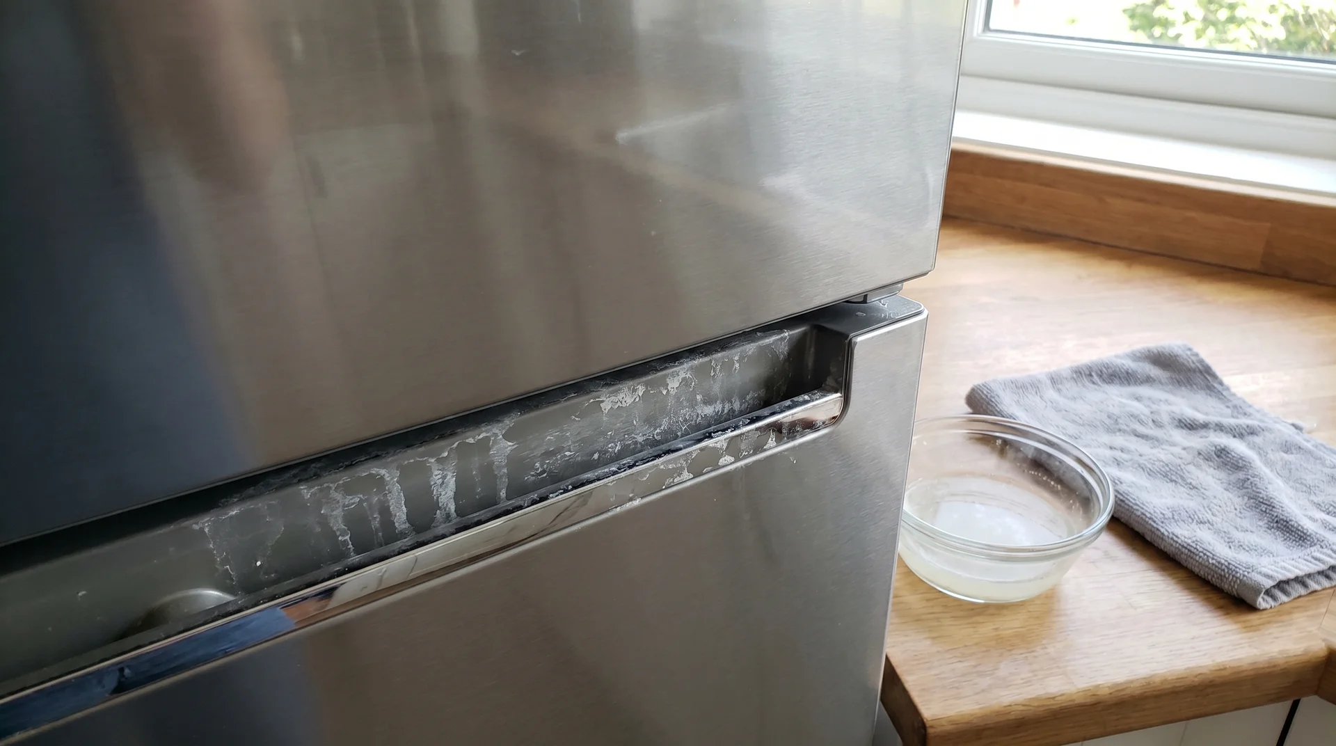 White hard water calcium deposits on stainless steel refrigerator door surface near bottom edge