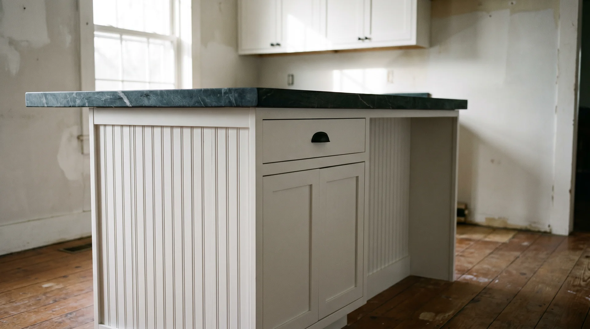 White shaker island base with beadboard end panels and dark soapstone countertop showing contrast in a real kitchen