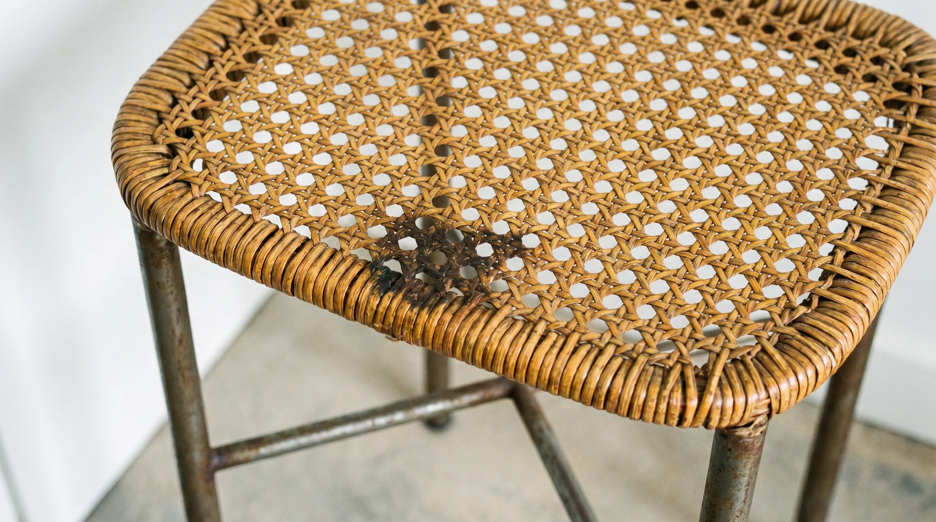 Woven rattan counter-height stool seat close-up showing natural fiber texture and grease stain near working kitchen edge